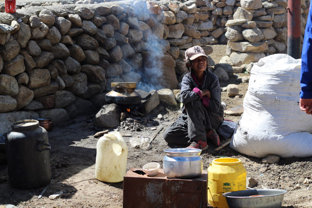 Donna intenta a cucinare all'aperto in un cortile di pietra durante un viaggio in Ladakh